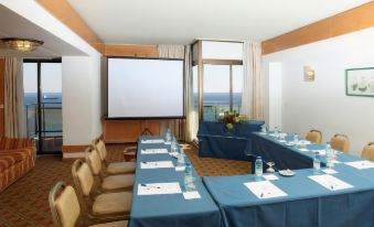 a conference room with blue tables , white chairs , and a projector screen , set up for a meeting at Hotel Estoril Eden