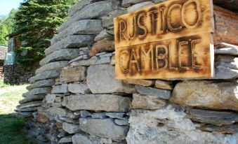 "a large stone wall with a wooden sign that reads "" rustico cambi "" on it , surrounded by greenery" at Camblee