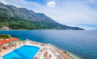 a large swimming pool is surrounded by lounge chairs and umbrellas , with mountains in the background at Tui Blue Makarska