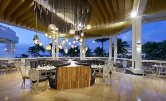 a modern restaurant with wooden tables and chairs , hanging light fixtures , and a view of the ocean at Grand Palladium Lady Hamilton Resort & Spa - All Inclusive