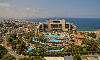 a large hotel with a pool and water slide is surrounded by palm trees and buildings at Le Royal Hotel - Beirut