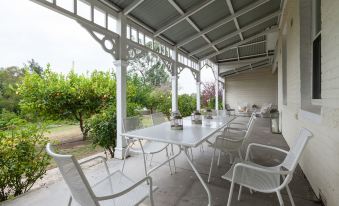 a white metal table and chairs on a covered patio , surrounded by greenery and trees at Yarra Gables