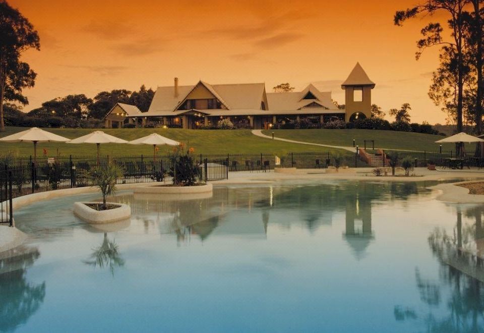 a large , ornate building with a pool in front of it , surrounded by trees and grass at BreakFree Raffertys Beach Resort