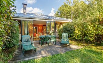 a small , cozy house with a wooden deck and green lawn furniture , surrounded by trees and grass at Center Parcs les Bois Francs