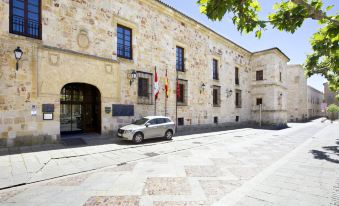 a brick building with a flag and a car parked in front , under a clear blue sky at Parador de Zamora