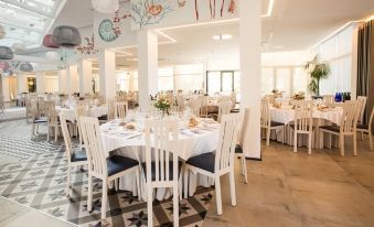 a large , well - decorated dining room with multiple round tables covered in white tablecloths and chairs arranged around them at Hotel Cap Negret