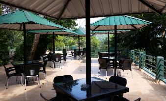 a patio area with several tables and chairs , some of which are covered by umbrellas at Rainforest Lodge, Deniyaya