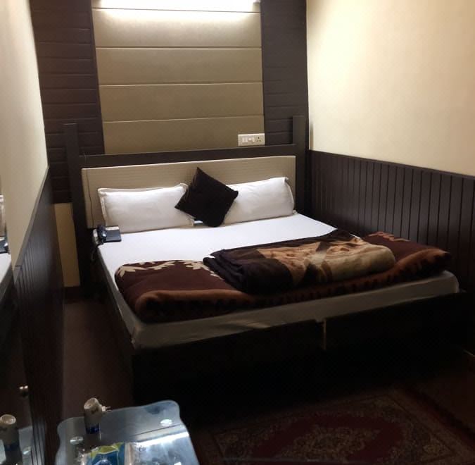 a bed with a brown headboard and white sheets is in a room with wooden walls at Hotel India