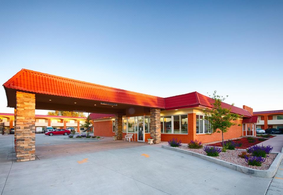 a red brick building with a red roof , situated next to a parking lot and surrounded by trees at LaJunta Inn