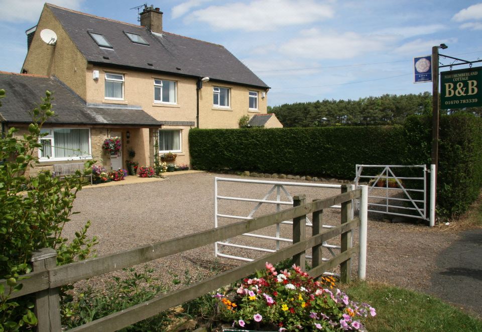 a rural setting with a white fence , gravel path , and flower garden , leading to a house with a brick foundation at Northumberland Cottage