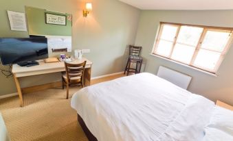 a well - lit bedroom with a bed , desk , and chair , as well as a window and door at The Woolpack Inn