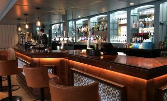 a well - stocked bar with a variety of liquor bottles and glasses , along with two bar stools at Hotel Wroxham