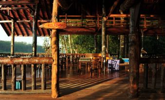an empty restaurant with wooden tables and chairs , surrounded by trees and a pool , under the light of the setting sun at Borneo Natural Sukau Bilit Resort