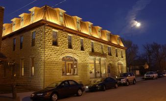 a large building with a brick facade and golden roof is illuminated by lights , surrounded by cars parked on the street at Midland Railroad Hotel