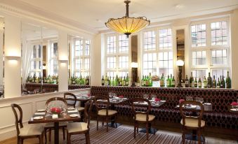 a well - lit dining room with large windows , wooden tables , and chairs , as well as several bottles of wine on display at Castle Hotel