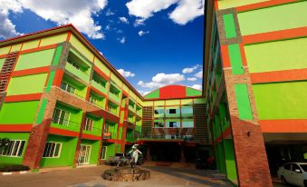 An apartment complex features a central courtyard adorned with vibrant buildings and a lush green lawn at Hiso Place Hotel