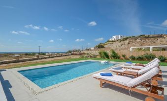 a large swimming pool surrounded by a patio , with several lounge chairs placed around it at Natura Villas in Naxos