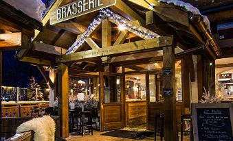 an outdoor restaurant with a wooden sign and a covered dining area , decorated with snow and lit up at night at Hotel Christiania