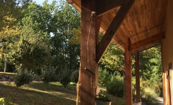 a wooden porch with a thatched roof overlooks a wooded area , surrounded by trees and bushes at Le Bellevue