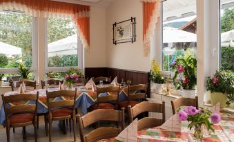 a restaurant with wooden tables and chairs , a flower arrangement , and large windows covered by orange curtains at Lotus