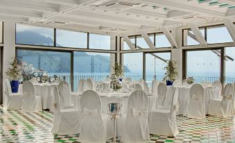 a large , empty banquet hall with white tablecloths and chairs set up for a formal event , overlooking a body of water at Hotel Miramalfi