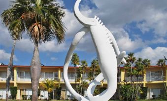 a large white sculpture of a lizard in front of a hotel , surrounded by palm trees at Colony
