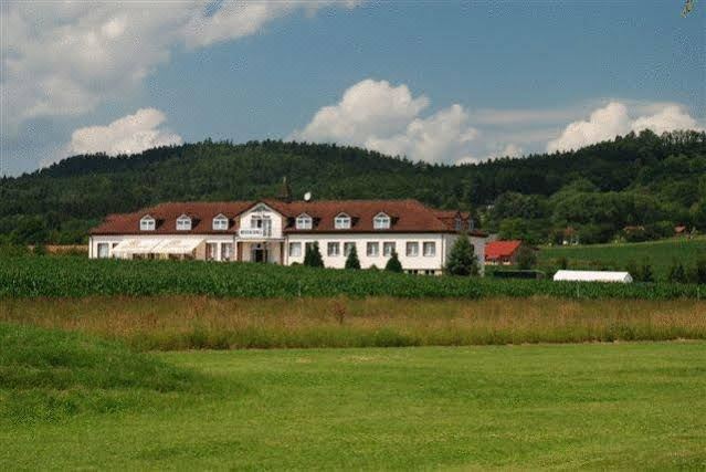 a large , white building with a red roof is surrounded by green grass and trees , set against a backdrop of mountains and a blue sky at Filip