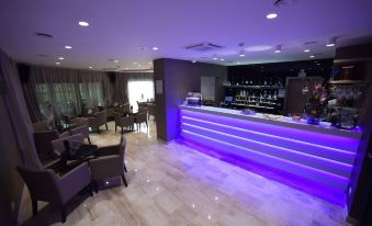 a bar area with a purple lighted counter and several chairs arranged around it , creating a welcoming atmosphere at Royal Airport Hotel