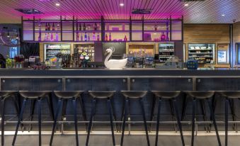 a bar with a row of stools in front of it , and a white swan figurine on the counter at Moxy Edinburgh Airport