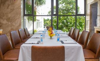 a long dining table with a white tablecloth and various items , including flowers , is set in a room with large windows at DTX Hotel Nha Trang