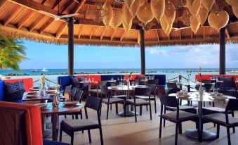 a restaurant with an open roof , wooden tables and chairs , and a view of the ocean at Renaissance Wind Creek Aruba Resort