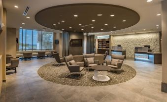 a modern lounge area with a circular seating arrangement and a large window overlooking the outdoors at SpringHill Suites Dallas Rockwall