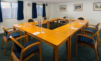 a conference room with a wooden table surrounded by chairs , water bottles , and blue curtains at Holiday Inn Express Stafford