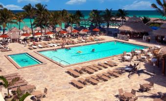 a resort pool area with lounge chairs , umbrellas , and people enjoying their time by the beach at Newport Beachside Hotel & Resort