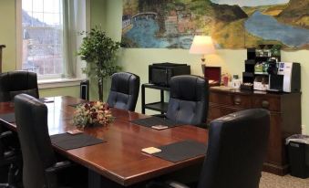 a conference room with a wooden table surrounded by black chairs , black leather cushions , and a large painting on the wall at The Inn at Stone Mill