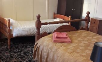 a cozy bedroom with two beds , one of which is made and the other has its sheets removed , along with a bedside table at Tudor House