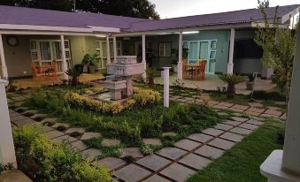 a house surrounded by a lush green garden , with several chairs and a dining table placed in the yard at Graceland Guesthouse