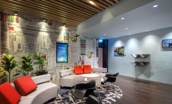 a modern lounge area with white couches , black chairs , and a red throw pillow on the couch at Ibis Melbourne Hotel and Apartments