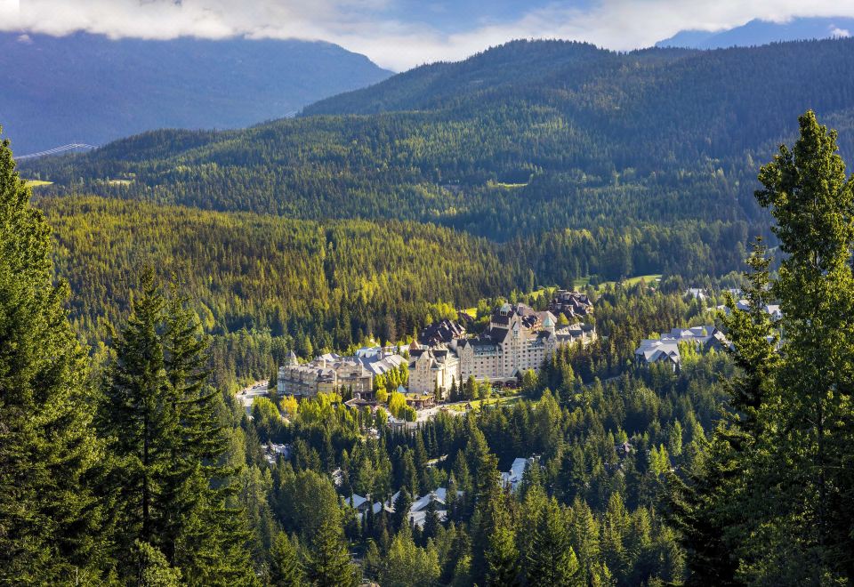 a picturesque mountain town nestled in a lush green forest , with a large building surrounded by trees and mountains at Fairmont Chateau Whistler