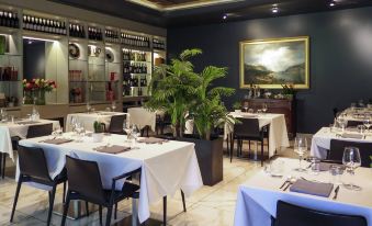 a modern restaurant interior with white tablecloths , black chairs , and green plants , set against a dark background at Ibis Styles Milano Est Settala