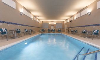 a large , empty swimming pool with blue water and white walls , surrounded by chairs and tables at TownePlace Suites by Marriott Champaign