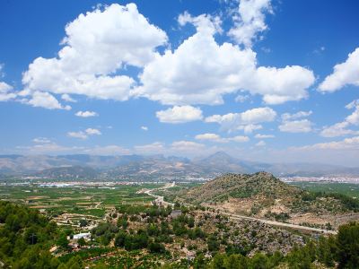 a picturesque landscape with a cloudy blue sky and green mountains in the background , and a winding road leading through the valley at Joli Joli Photo