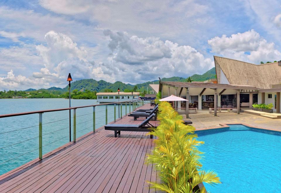 a large wooden deck overlooking a body of water , with several lounge chairs and umbrellas placed around the pool area at Novotel Suva Lami Bay