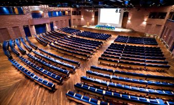 an empty auditorium with rows of blue chairs and a stage at the front , likely for an event or meeting at Renaissance Tuscany Il Ciocco Resort & Spa