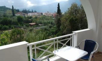 a balcony overlooking a scenic view of mountains and trees , with a table and chairs set up for outdoor dining at Koukounaria Hotel & Suites