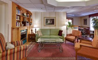 a cozy living room with a green couch , wooden chairs , and a fireplace , along with a red carpet and bookshelves at La Quinta Inn & Suites by Wyndham Knoxville North I-75