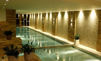 an indoor swimming pool surrounded by lounge chairs , with several people enjoying their time in the water at Santa San