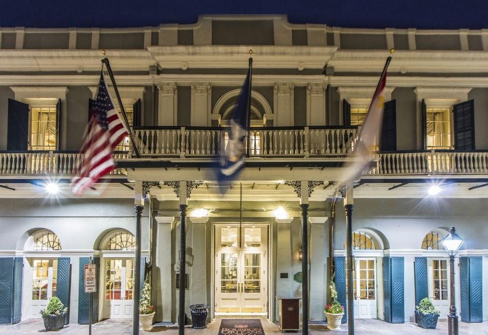 a large white building with multiple american flags hanging from the balcony , creating a festive atmosphere at Bourbon Orleans Hotel
