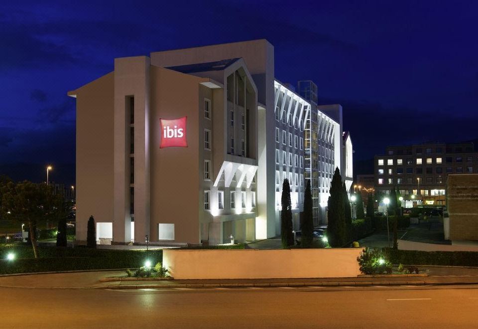 a large building with a red sign on the side is lit up at night at Ibis Firenze Nord Aeroporto