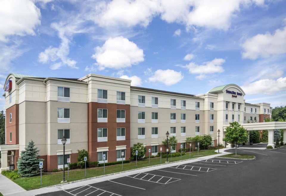 a large hotel with a parking lot in front of it , surrounded by grass and trees at SpringHill Suites Long Island Brookhaven